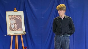18.	Młody chłopak w ciemnej koszuli i szarych spodniach, z lewej strony portret.