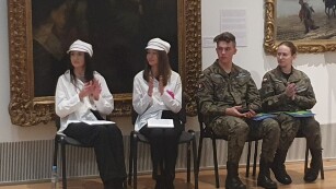 Siedzą dwie młode dziewczyny w czapkach Arciszanek, dziewczyna i chłopak w mundurze moro