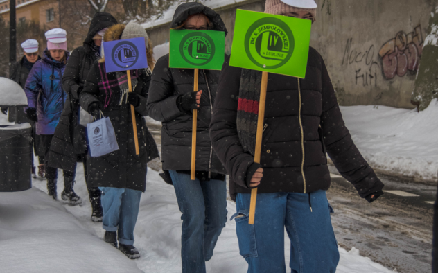 Grupa młodych ludzi z tabliczkami IV LO, w czapkach Arciszanek schodzi po zaśnieżonym chodniku ulicy Szkolnej