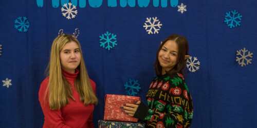 Dwie dziewczyny z paczkami prezentów, w tle granatowa ścianka z napisem Mikołajki