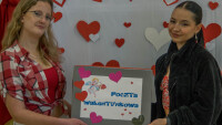 Dwie dziewczyny na tle dekoracji walentynkowej, w rękach trzymają napis Poczta Walentynkowa