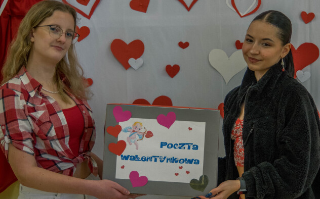 Dwie dziewczyny na tle dekoracji walentynkowej, w rękach trzymają napis Poczta Walentynkowa