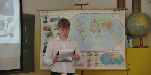 Młody chłopak w białej koszuli czyta tekst, w tle mapa świata i globus