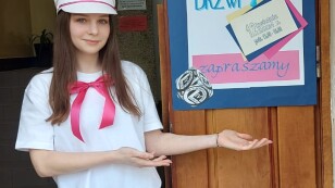 Dziewczyna w czapce Arciszanki i w białej bluzce, zaprasza do szkoły na dzień otwarty